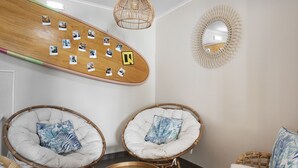 Een kamer met twee rieten stoelen, een houten plank met foto's, een spiegel en een geweven lamp.