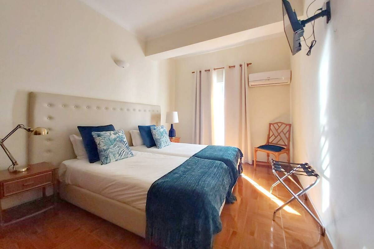 Un lit double avec une tête de lit, une lampe de chevet, une chaise et un appareil de climatisation.