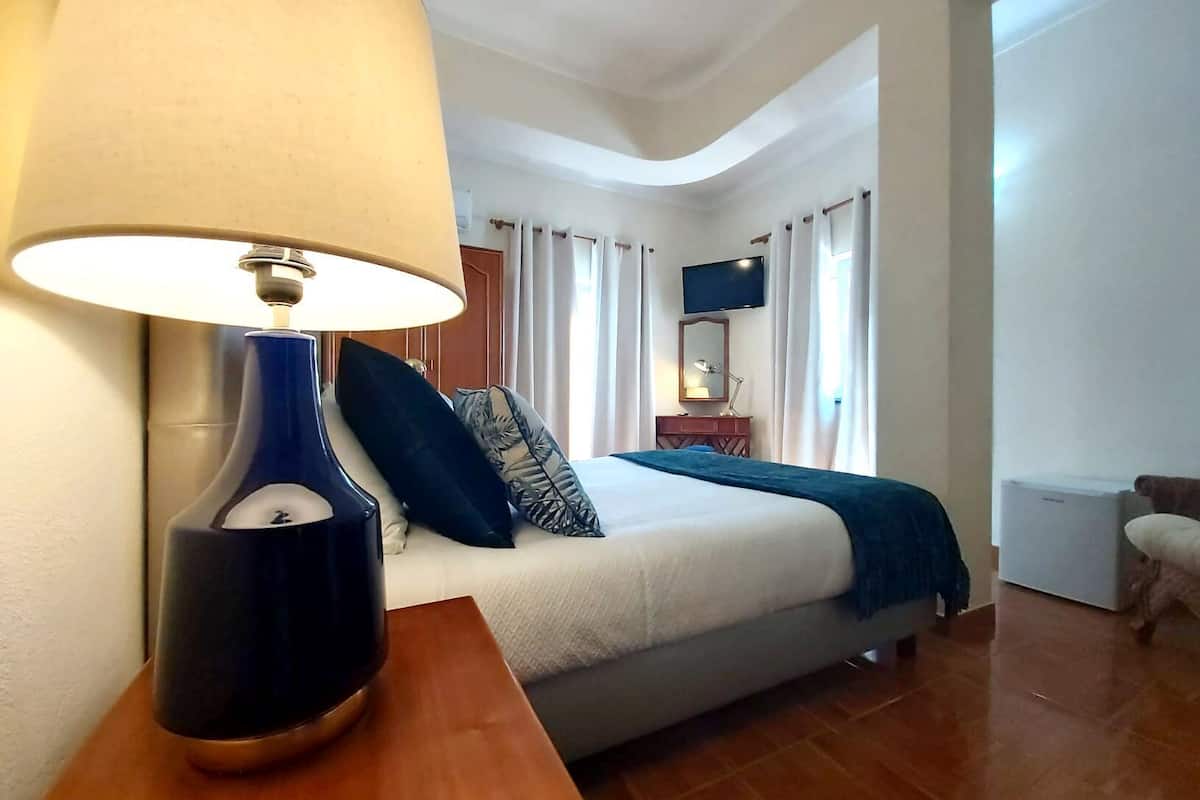 Une chambre d’hôtel avec un lit, une table de chevet avec une lampe, une télévision et un petit bureau avec un miroir.