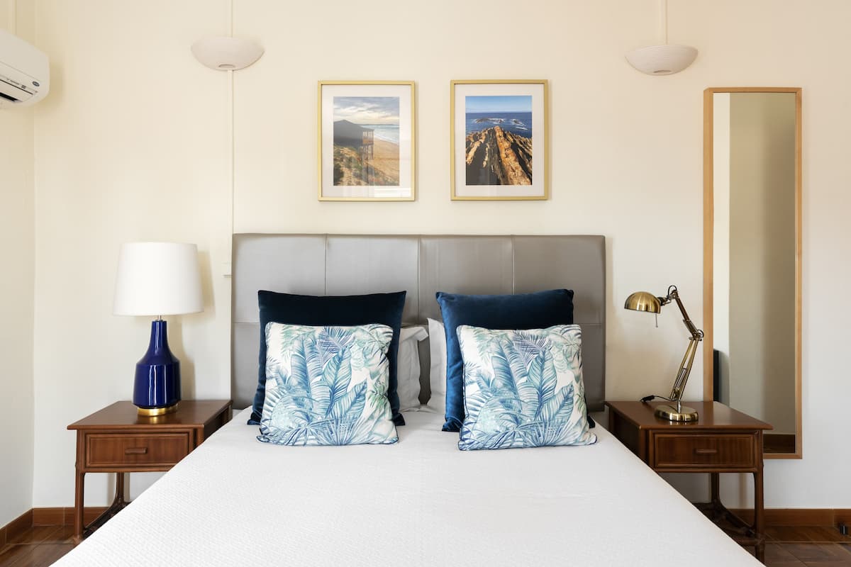 Une chambre d’hôtel avec un grand lit, deux tables de chevet, un bureau, un miroir et deux tableaux encadrés au mur.