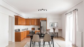 A modern kitchen with wooden cabinets, a dining table with chairs, and a large window with curtains. - Superb & Comfy 2 BD Apartment in Marousi (Marousi)