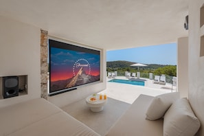 A modern outdoor seating area with a pool, a mounted television, and a clear view of a mountainous landscape. - Exclusive Casa Mir located in 'el Vila' with Pool & with all amenities (Puerto Pollensa)