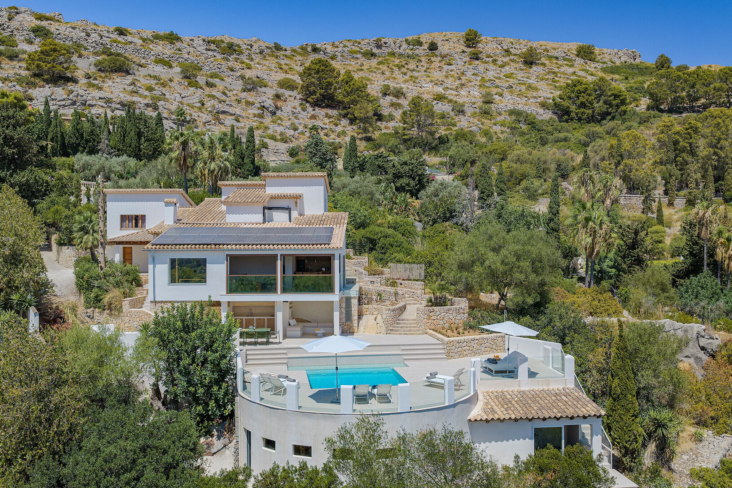 A modern two-story house with a rooftop pool and a view of a hilly landscape.