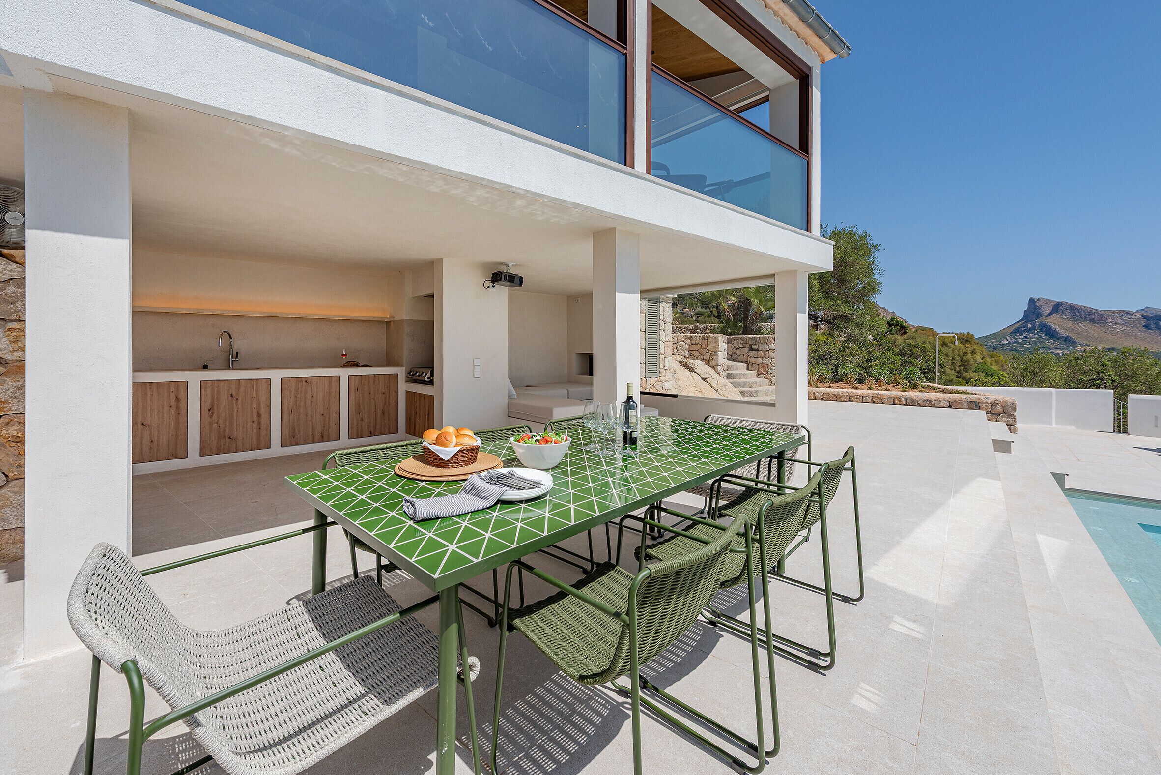 Un espace de repas extérieur moderne, doté d’une piscine, d’une cuisine et offrant une vue sur les montagnes.