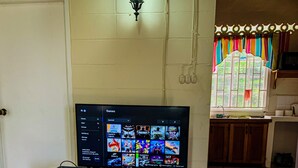 A room with a television on a cabinet, a window with colorful curtains, and a tiled floor.