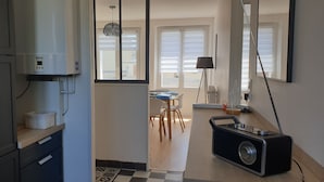 Kompakti keittiö, jossa on jääkaappi, pesukone sekä ruokailutila pöytineen ja tuoleineen.