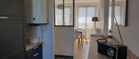 Een kleine keuken met een koelkast, een wasmachine en een eethoek met een tafel en stoelen.