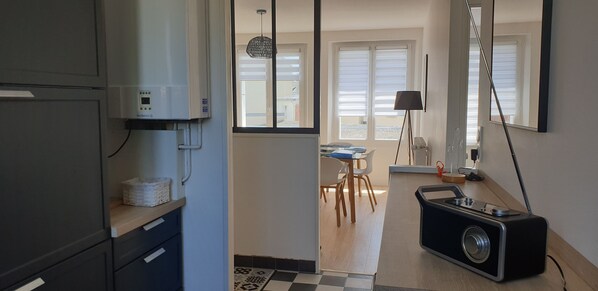 A compact kitchen with a refrigerator, a washing machine, and a dining area with a table and chairs.