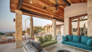 An outdoor patio area with a wooden ceiling, stone pillars, a green sofa, a grey sofa, and a round table. - Villa Elea, New Deluxe Golf Villa in Aphrodite Hills - 6 Bedrooms, 7 Bathrooms.  (Kouklia)