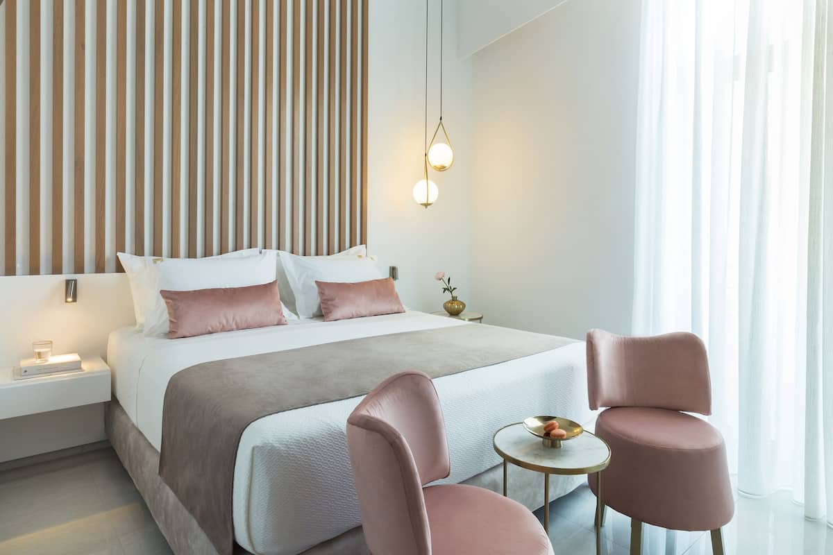 A modern hotel room with a large bed, bedside tables, a small round table, and two chairs.