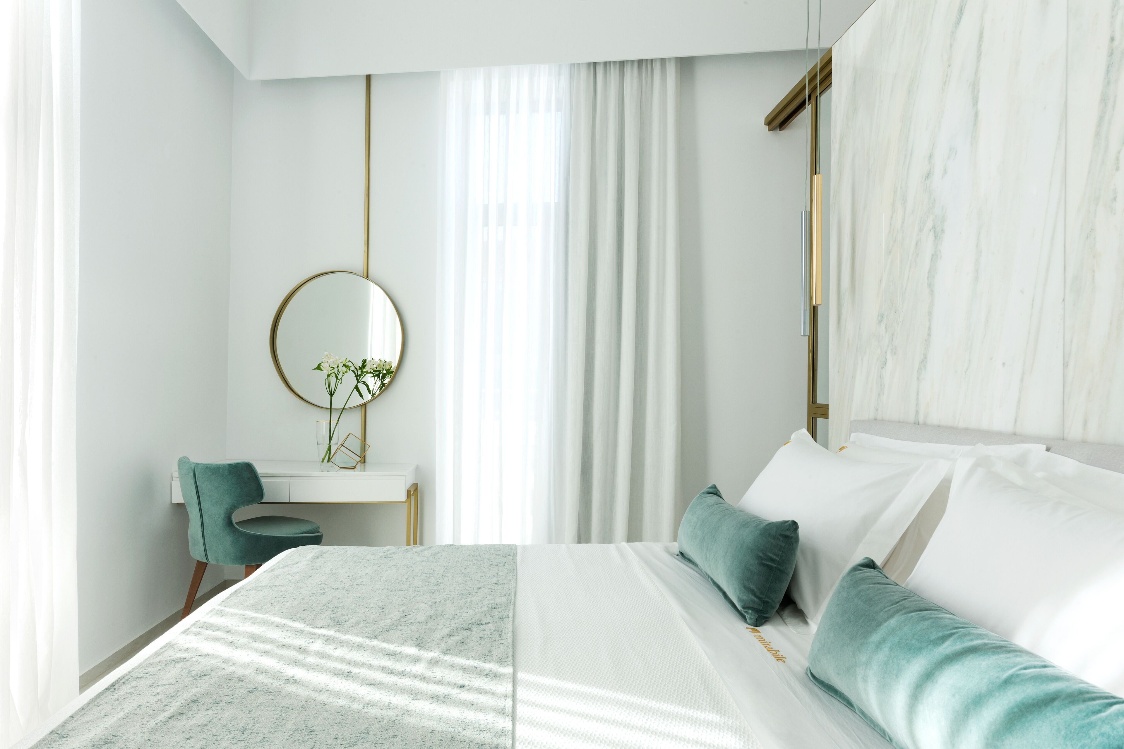 A modern bedroom with a large bed, a desk with a chair, a round mirror, and a window with curtains.