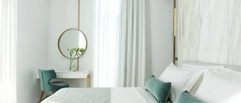 A modern bedroom with a large bed, a desk with a chair, a round mirror, and a window with curtains.