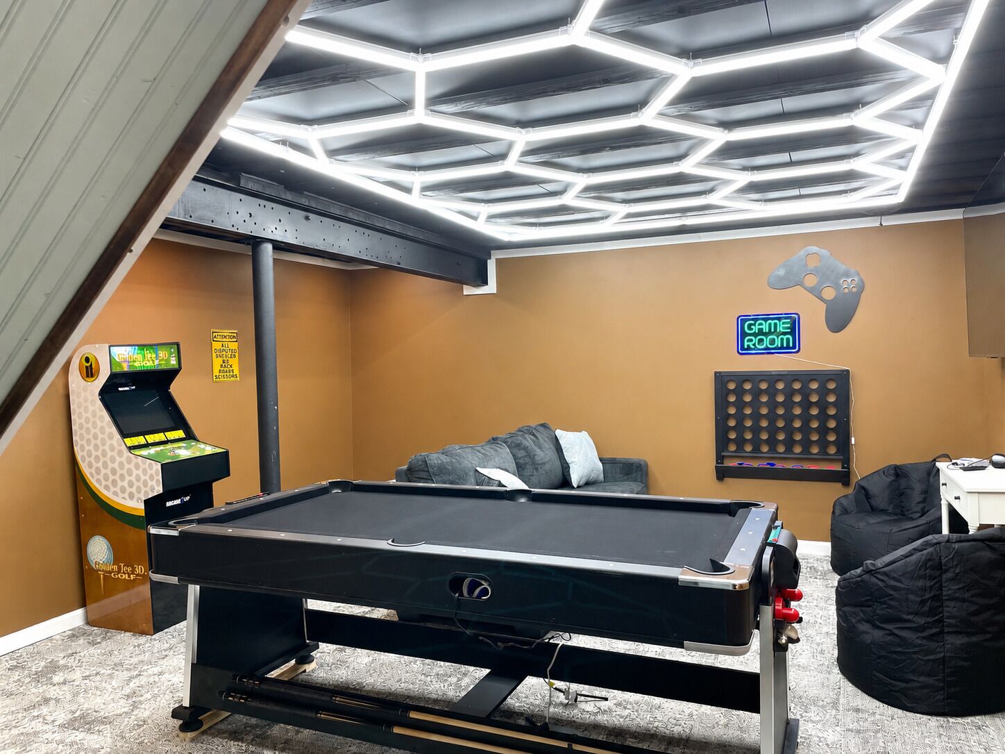 Une table de billard dans une pièce dont le plafond présente un motif hexagonal, avec un panneau indiquant l’espace de jeux et une table de billard de la marque « Golden Tee 3D Golf ».