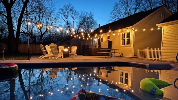 Un jardin avec une piscine, des chaises longues et des guirlandes lumineuses.