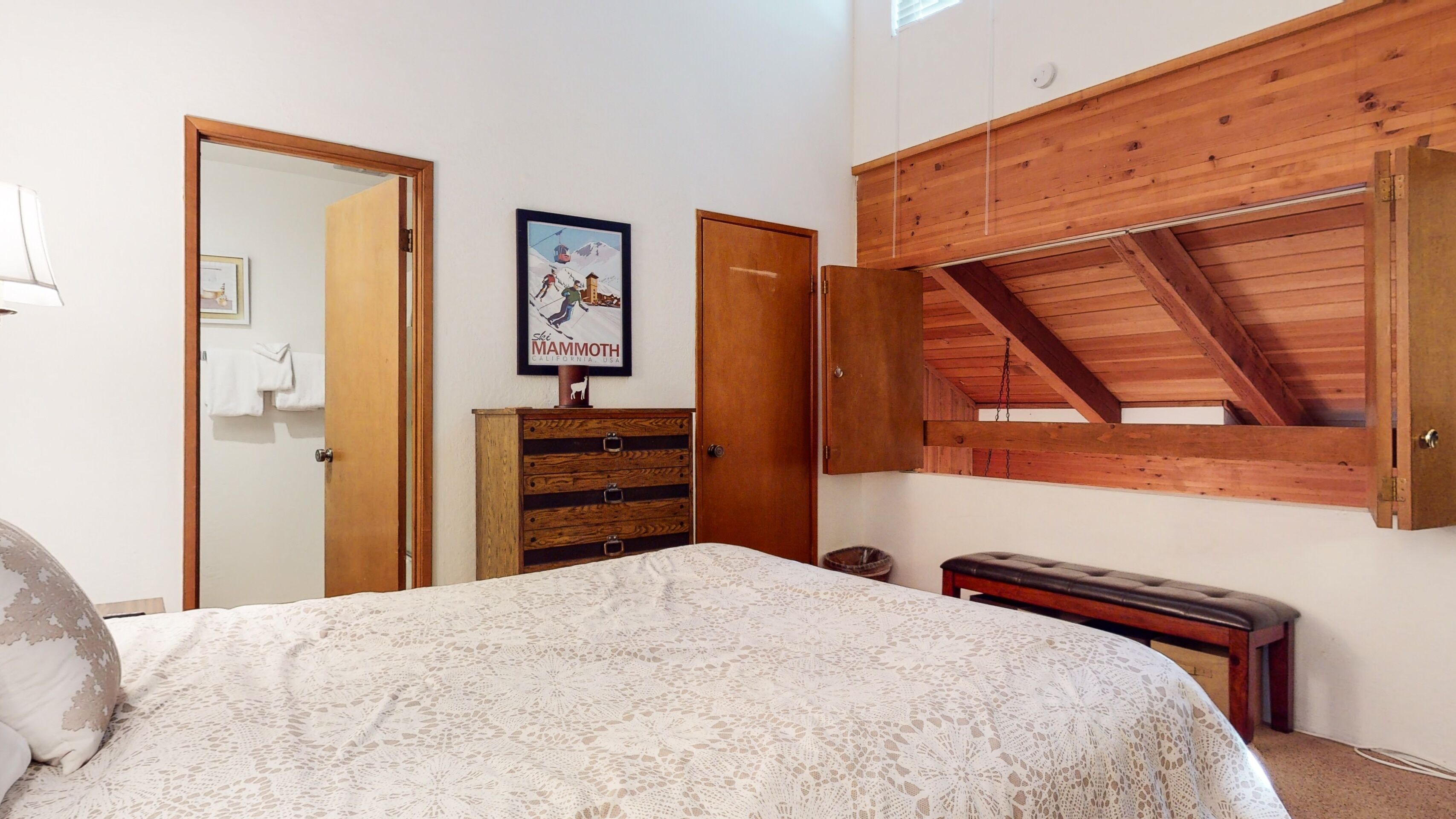 A bedroom with a bed, wooden dresser, and a lofted wooden ceiling.