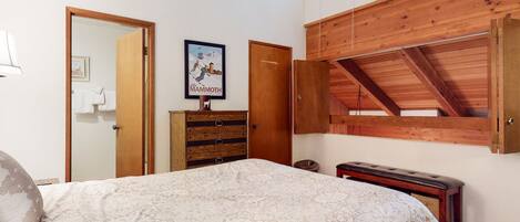 A bedroom with a bed, wooden dresser, and a lofted wooden ceiling.
