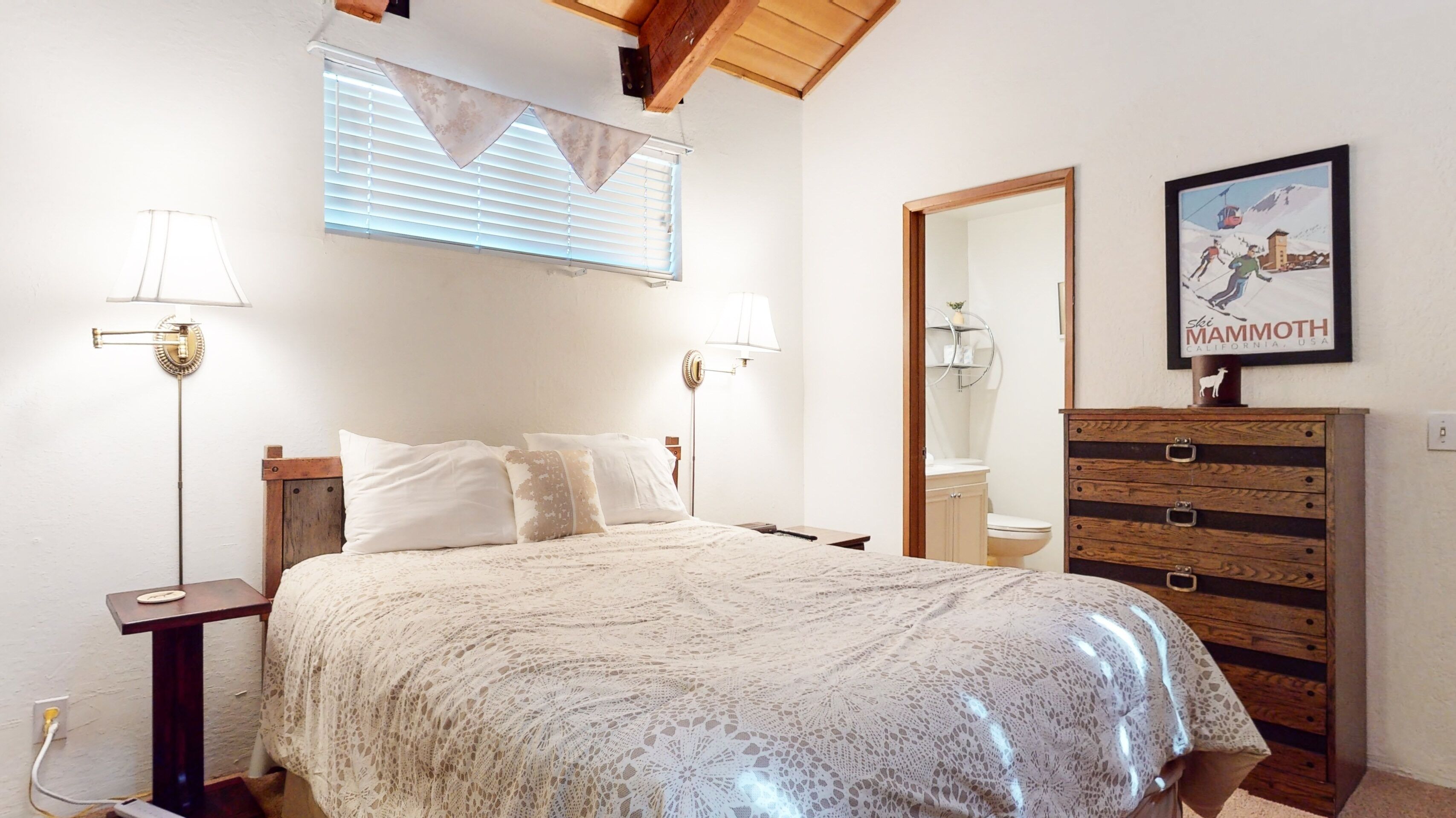 Quarto com cama, abajures, penteadeira, espelho e um pôster na parede.