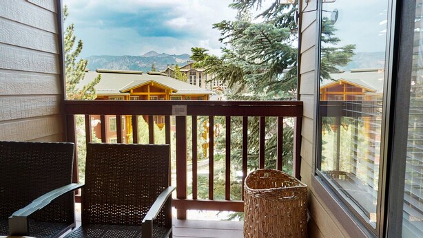 Un balcón con mobiliario de mimbre y una cesta de mimbre, con vistas a montañas y edificios.