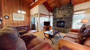 Una sala acogedora con chimenea de piedra, vigas de madera, televisor y asientos cómodos.