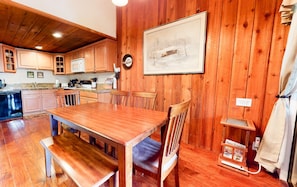 Un intérieur en bois comprenant une table et des chaises, un coin cuisine avec des placards et des appareils électroménagers, et un tableau encadré accroché au mur.
