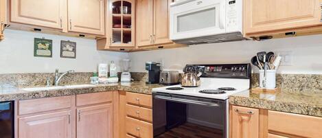 A kitchen with wooden cabinets, a microwave, a stove, a sink, and various appliances.