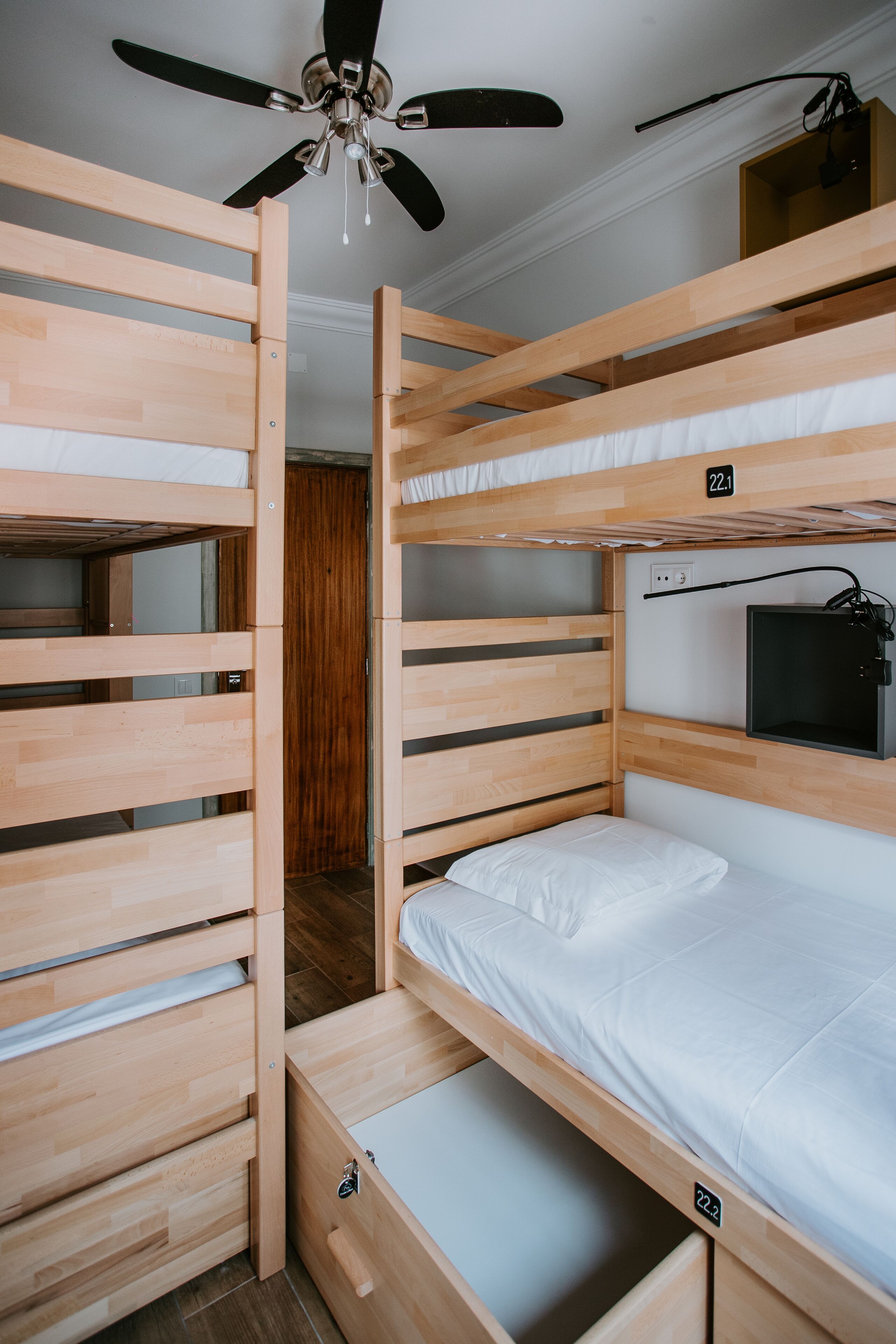 A bunk bed room with a ceiling fan, a TV mounted on the wall, and a wooden door.