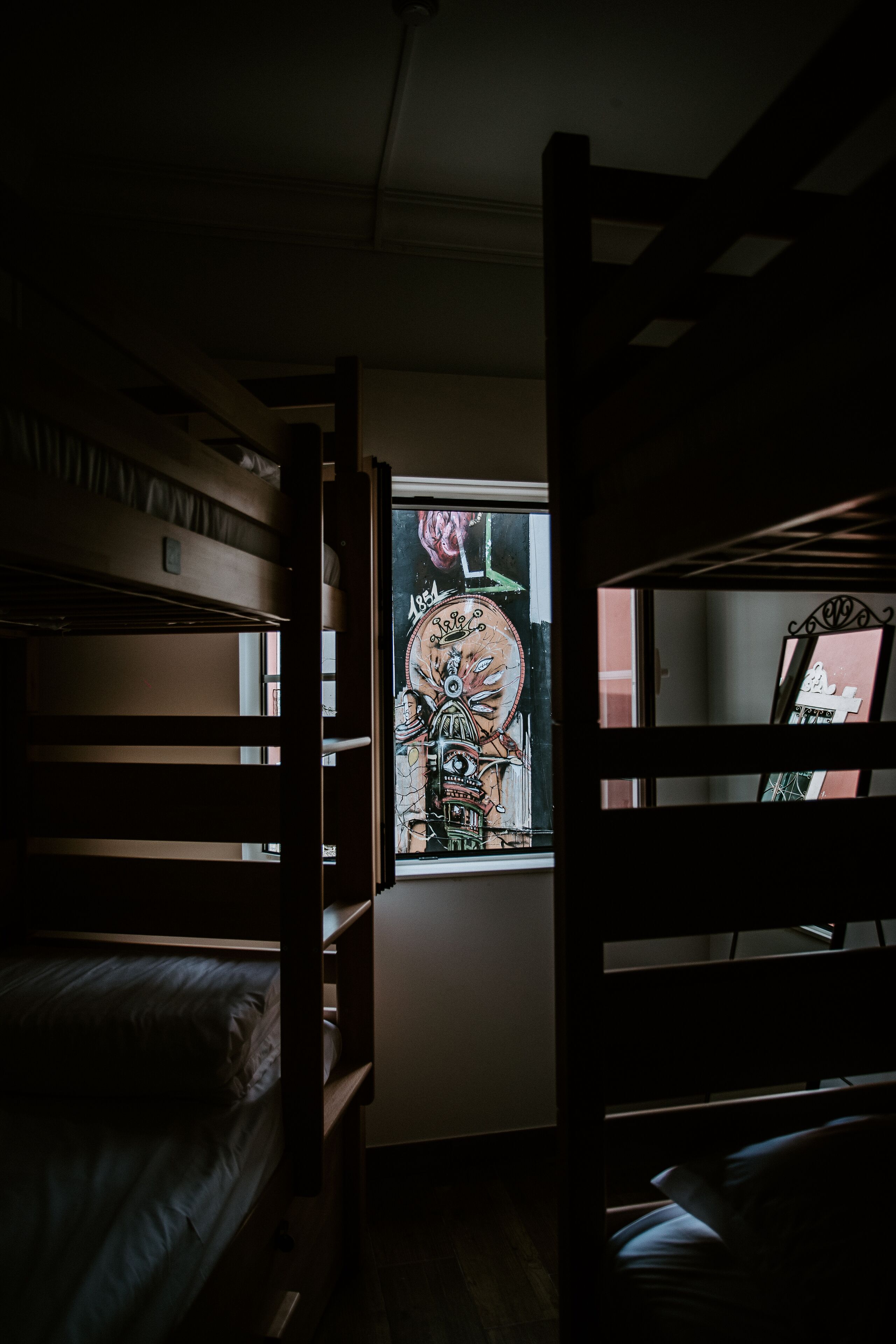 Una habitación tenuemente iluminada con literas y una ventana decorada con un mural colorido.