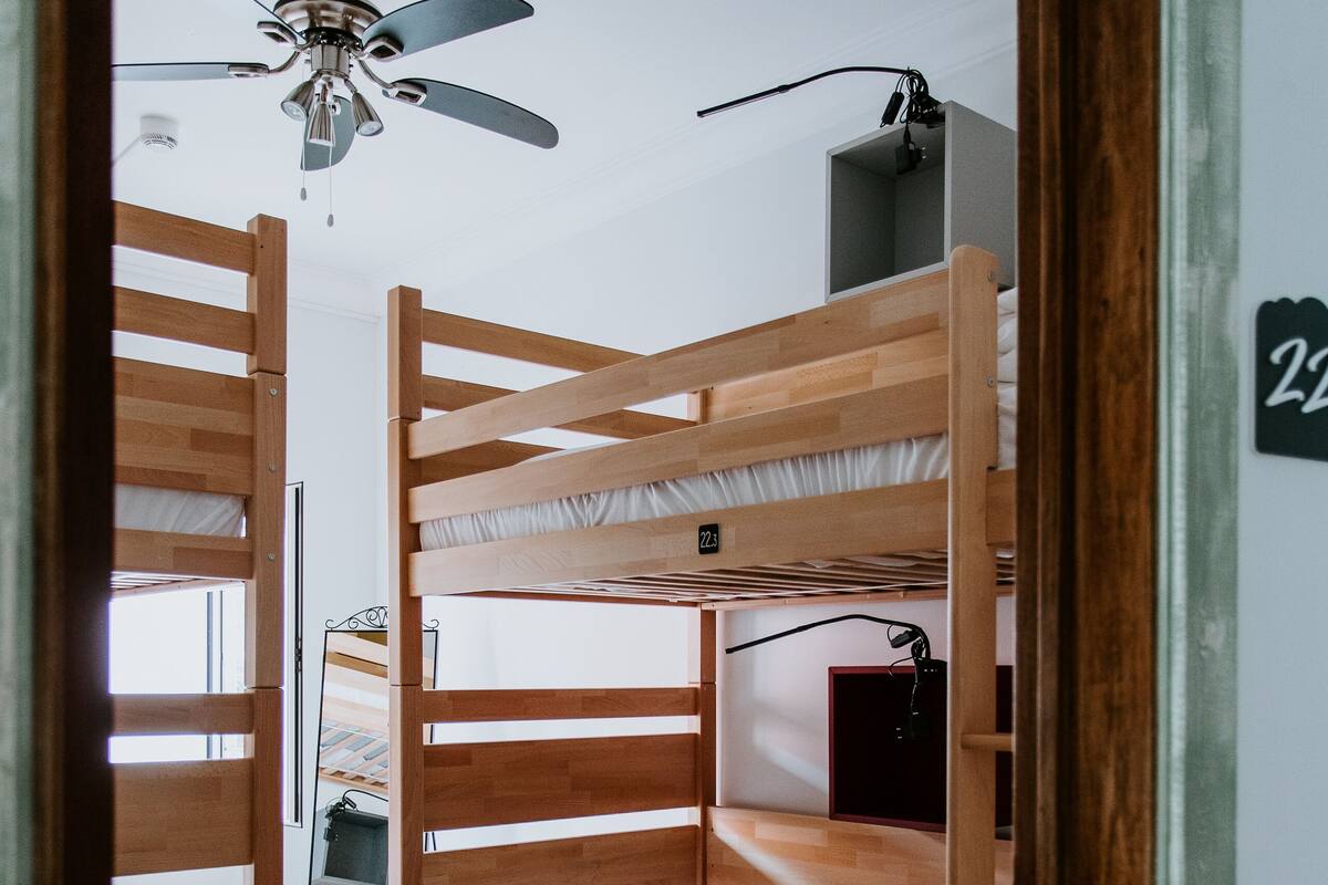 A bunk bed room with a ceiling fan, a small desk, and a mirror.