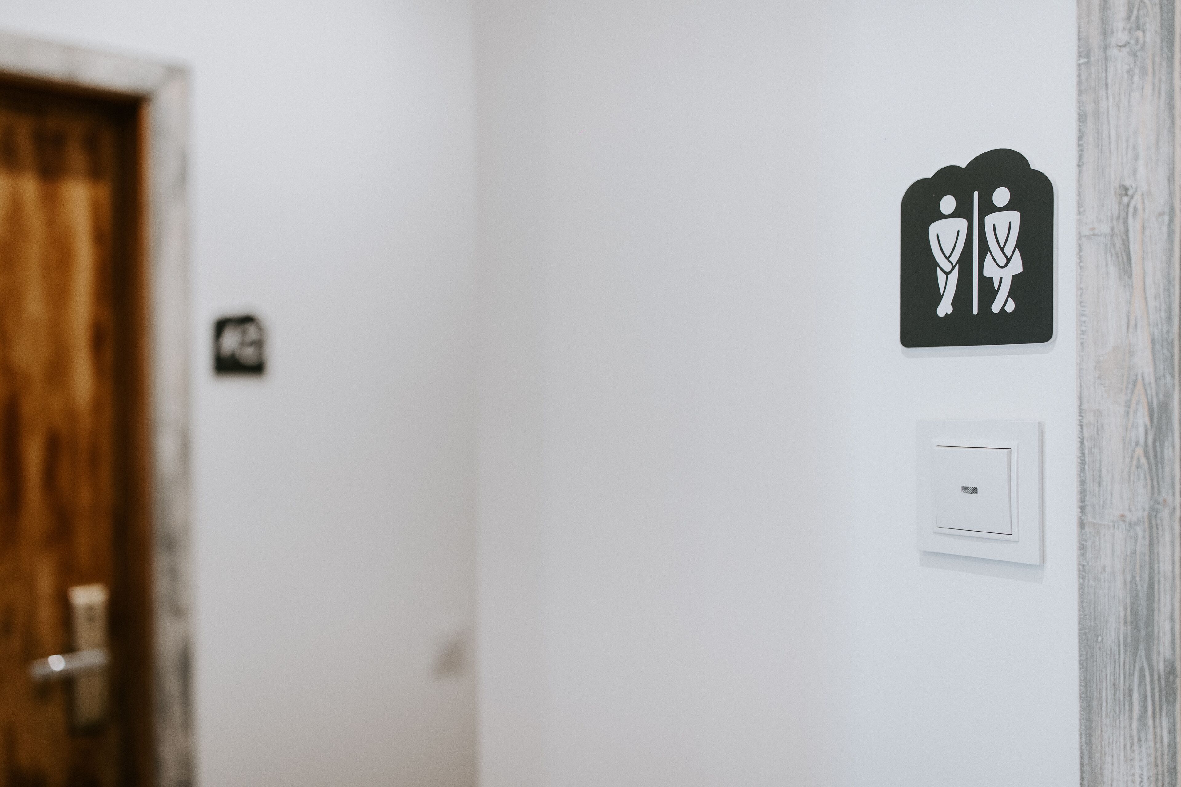 Un letrero de baño con símbolo de hombre y mujer, una puerta y un interruptor de luz en la pared.