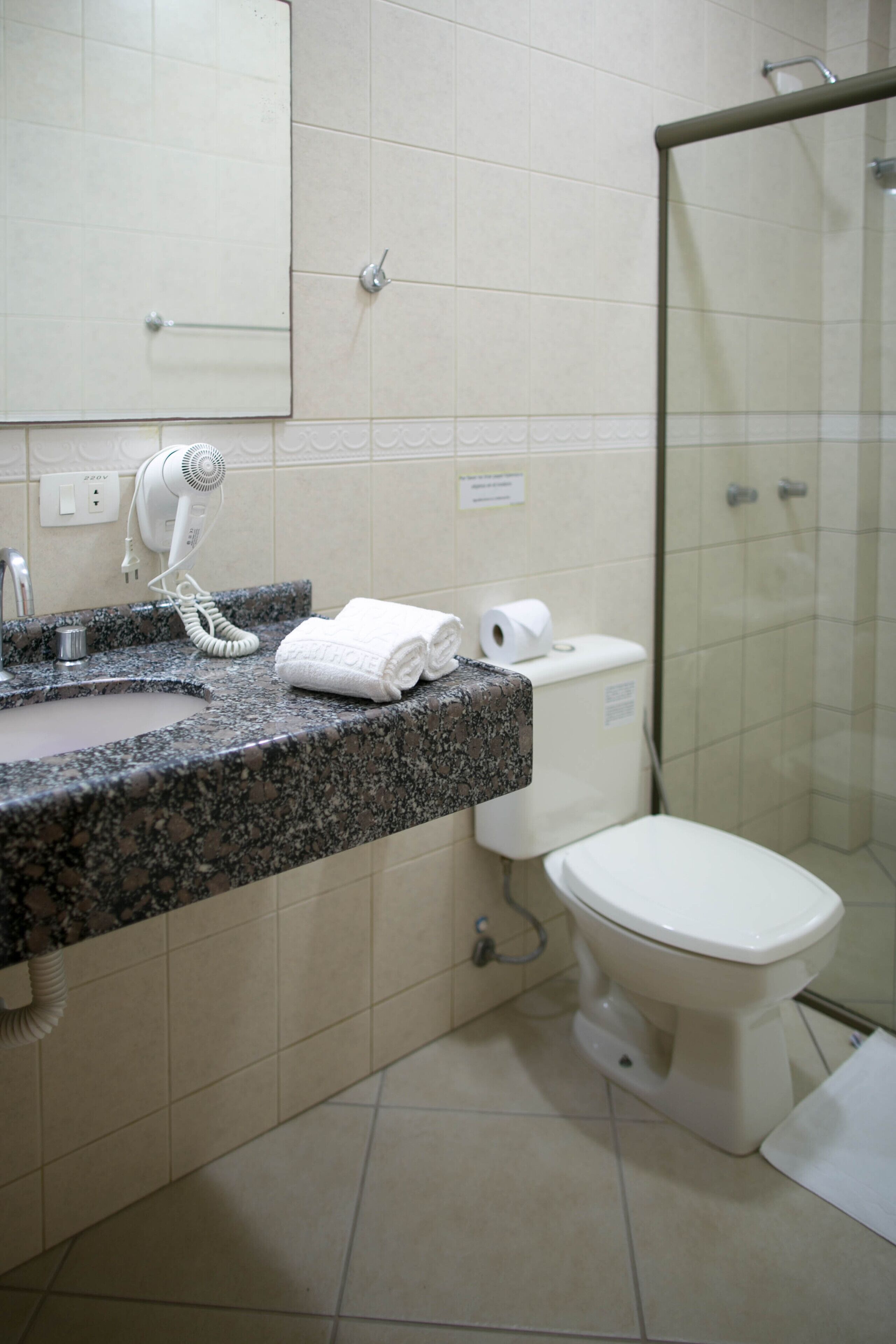 Un baño con encimera de granito, un lavabo blanco, un secador de pelo, una toalla y un inodoro.