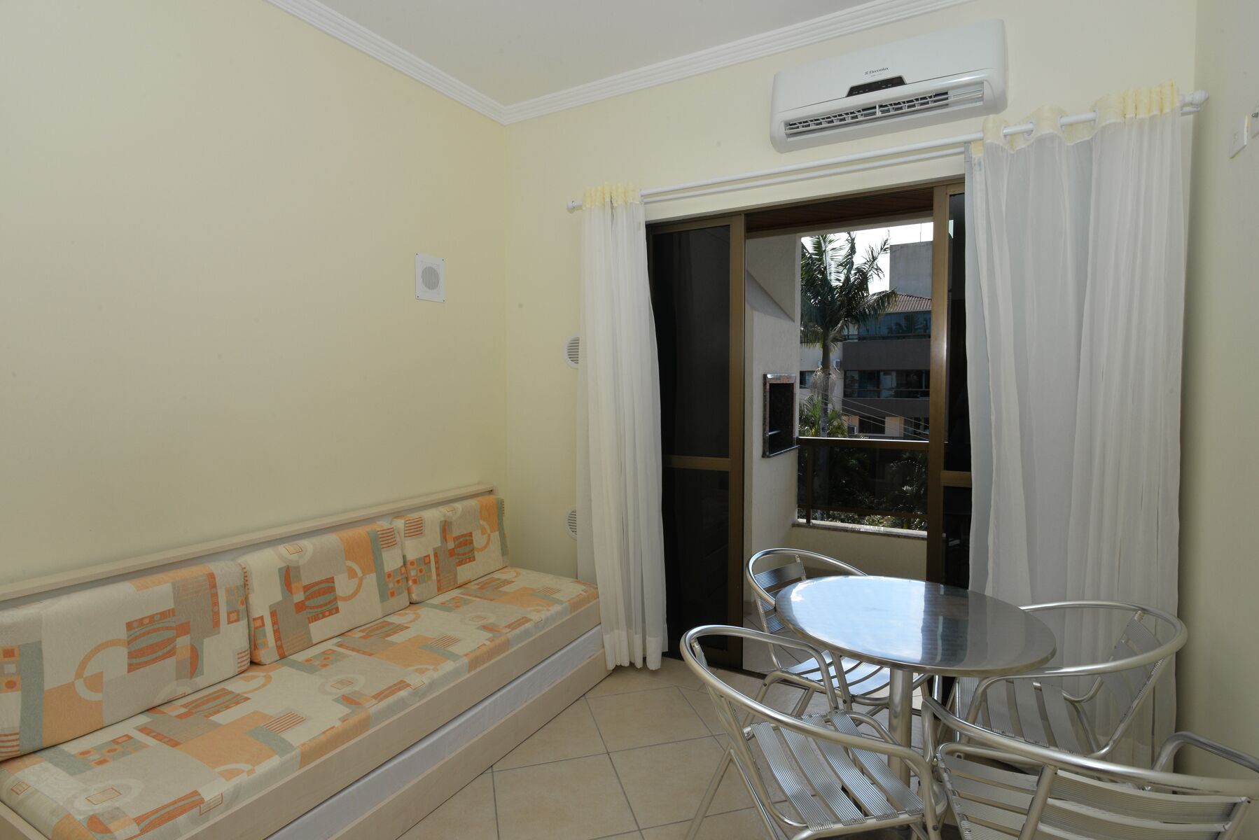 Una habitación con sofá, una mesa y sillas, aire acondicionado y vistas por una puerta.