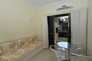 Una stanza con un divano, un tavolo con sedie, un condizionatore d'aria e vista attraverso una porta.