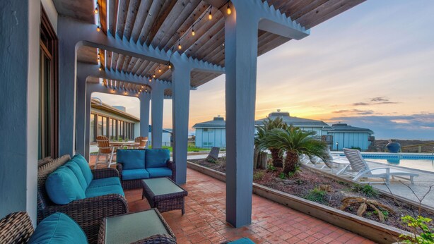A covered outdoor seating area with wicker furniture and a view of a pool and buildings in the background. - Beach Access! Heated Community Pool! Float in the pool while looking at the beac (Port Aransas)