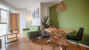 Una sala de estar moderna con un sofá verde, una mesa de comedor redonda de madera y una lámpara colgante.
