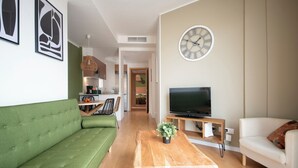 Una sala de estar moderna con un sofá verde, una mesa de centro de madera, un televisor sobre un mueble de madera y un reloj en la pared.