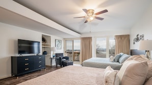 Ein Schlafzimmer mit einem großen Bett, einem Schreibtisch, einem Sessel, einem Fernseher und einem Deckenventilator.