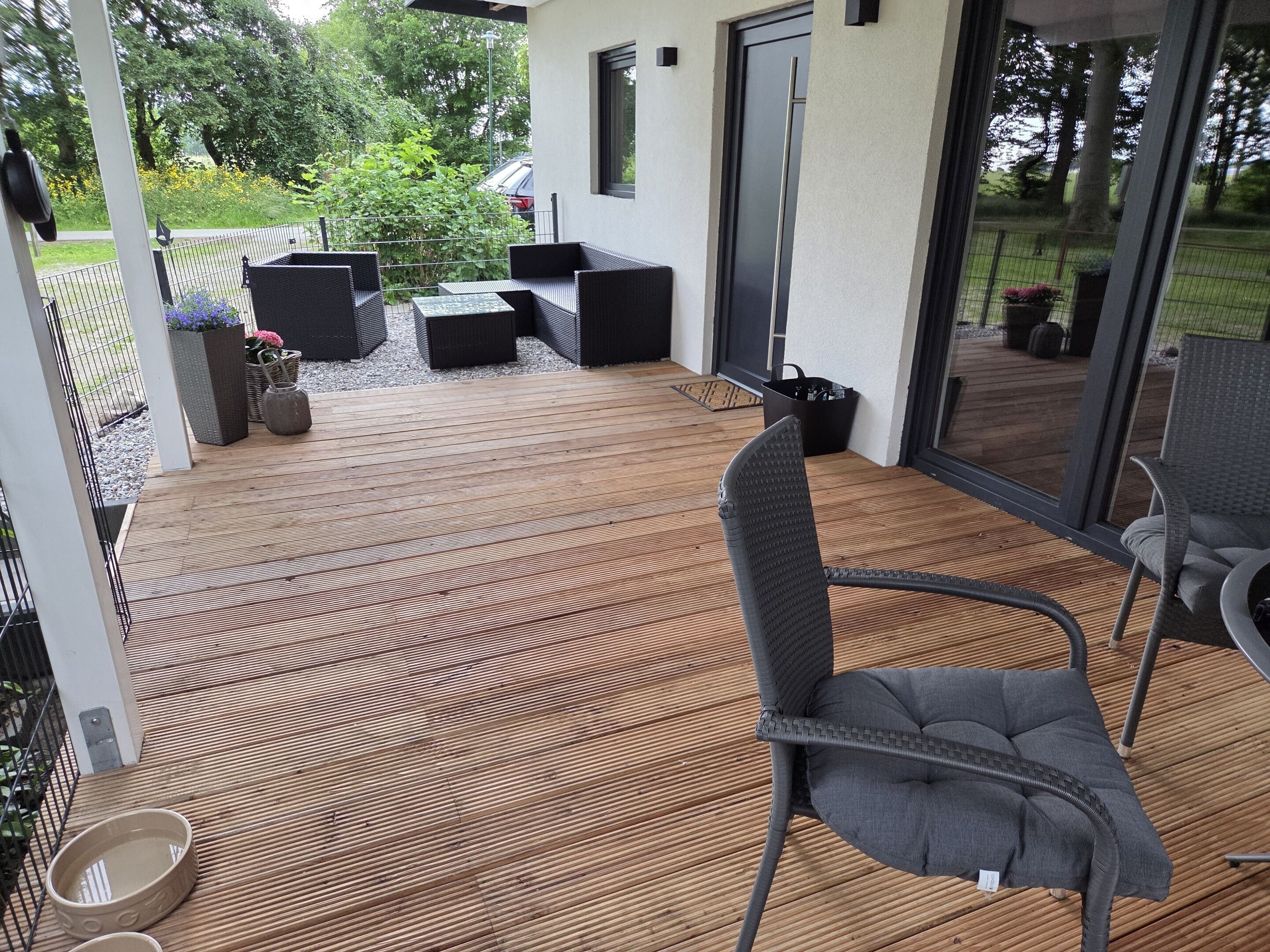 Eine überdachte Terrasse mit Gartenmöbeln, ein Holzdeck und Blick ins grüne Umland.