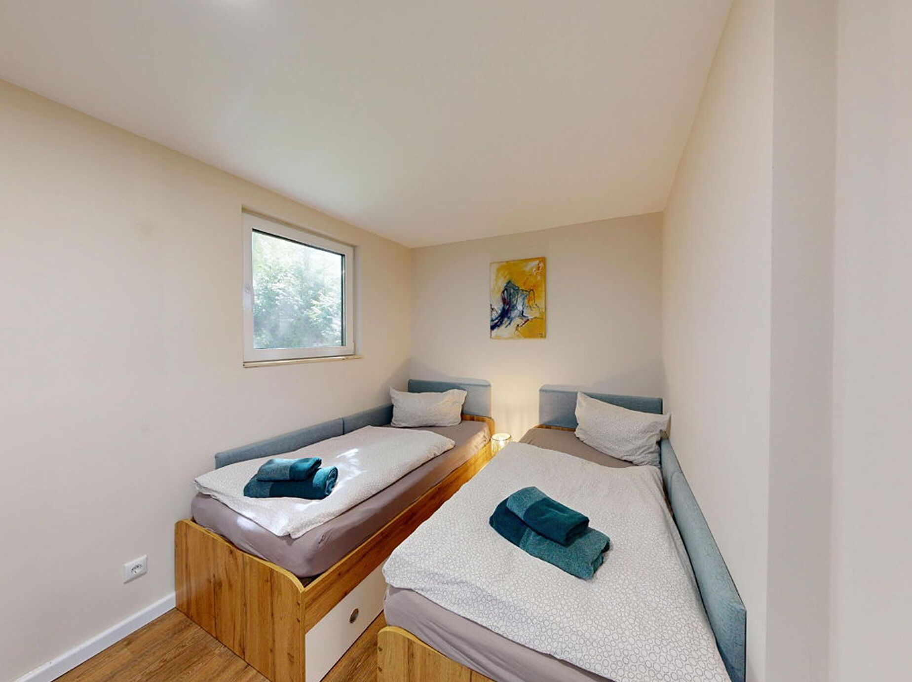 Quarto pequeno e moderno com duas camas de solteiro, uma janela e um quadro na parede.