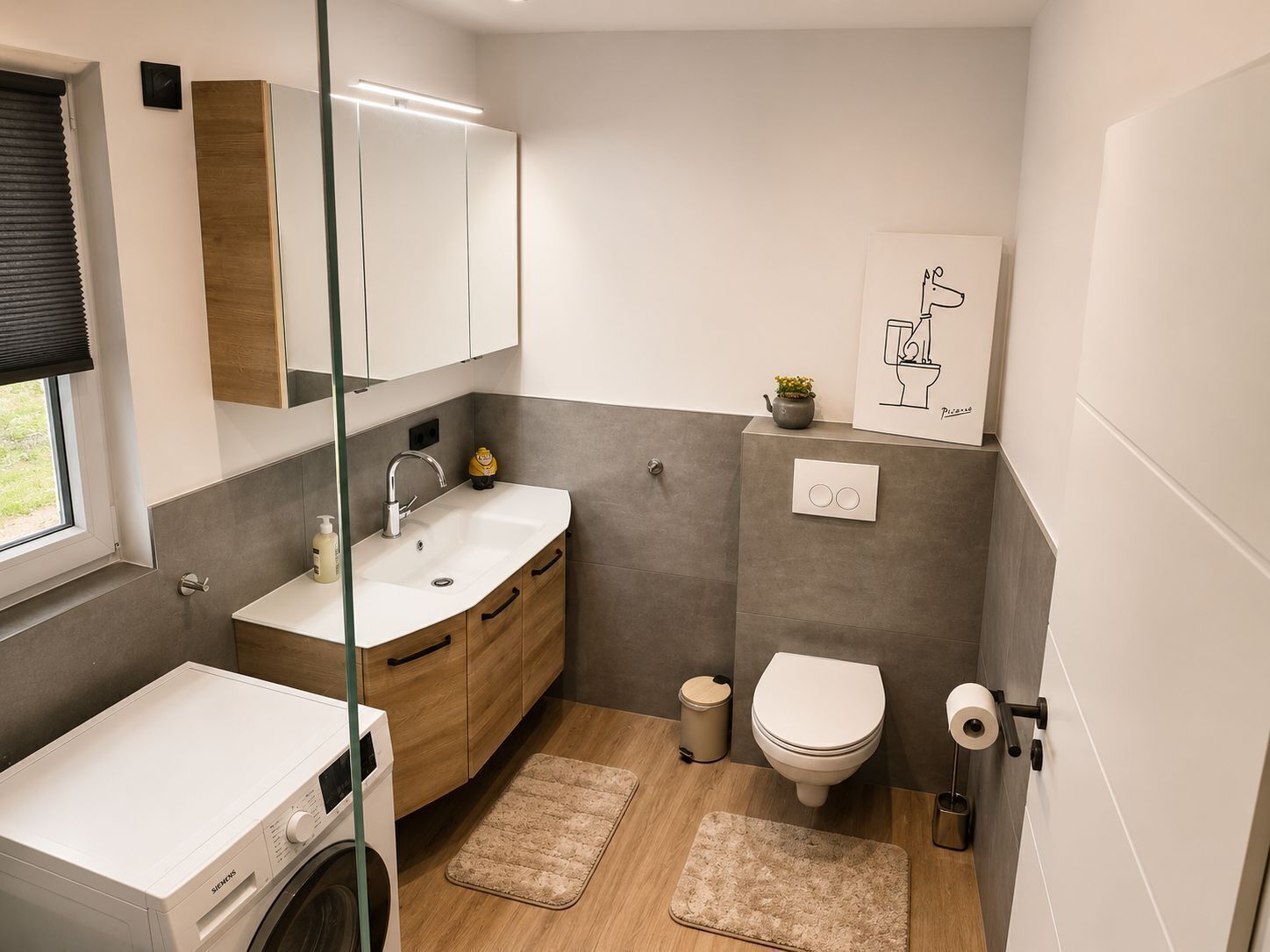 A compact bathroom with a washing machine, a sink, a toilet, and a small potted plant.