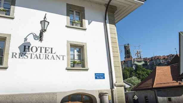 Un bâtiment blanc avec une enseigne indiquant « HÔTEL-RESTAURANT » et une autre, bleue, indiquant « Place Sphirvere Obere Matte ».