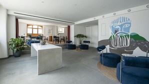 Un vaste espace de vie comprenant une table basse centrale, des fauteuils recouverts d’un tissu bleu et une grande fresque abstraite sur le mur.
