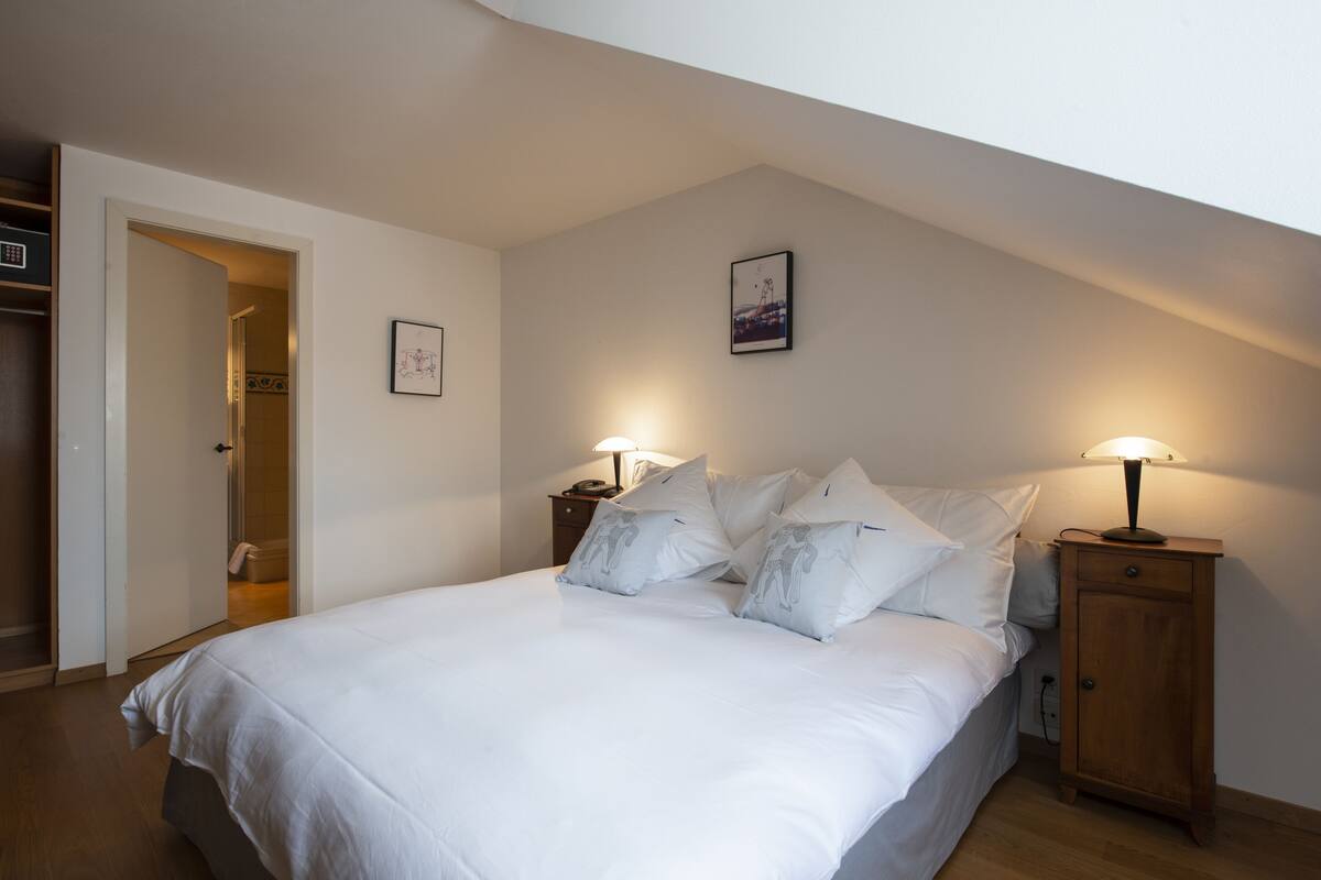 Une chambre à coucher avec un grand lit, deux tables de chevet avec des lampes, une armoire et une porte donnant sur une autre pièce.