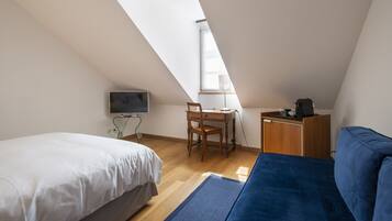 Une petite pièce bien éclairée, avec un lit, un bureau et une chaise, un canapé et un téléviseur.