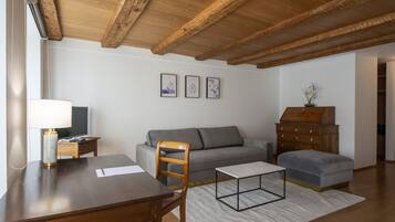 A modern living room with a wooden ceiling, a grey sofa, a wooden dining table, and a small side table with a lamp.