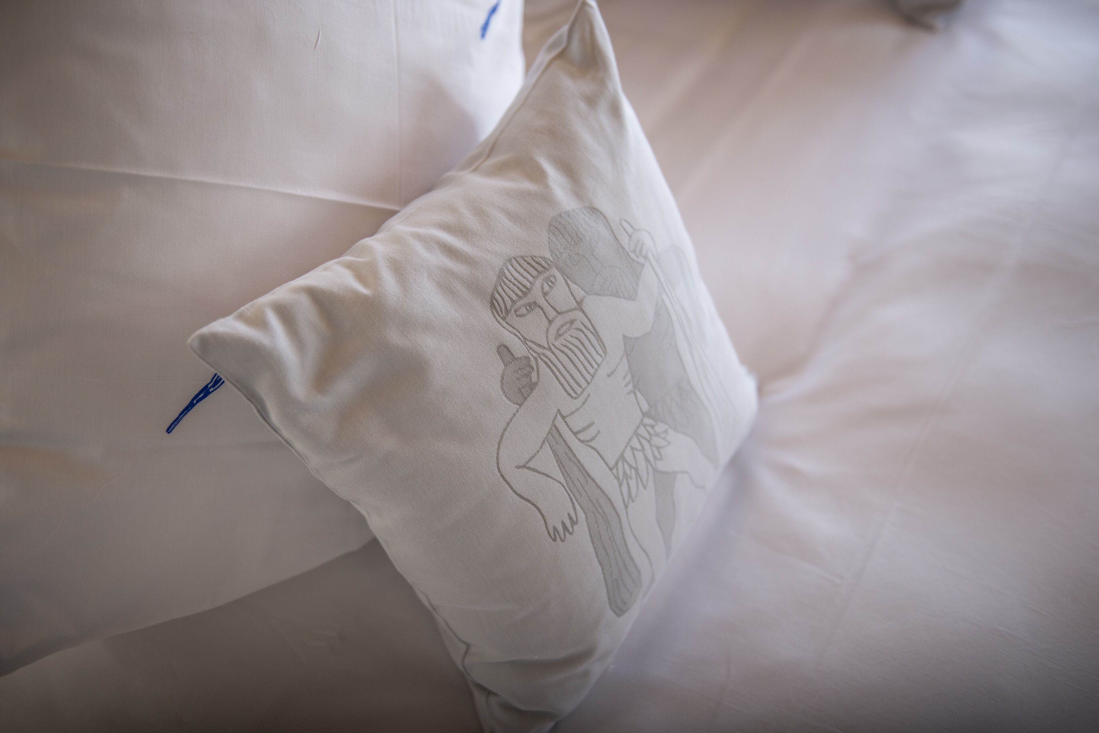 Ein Kopfkissen mit einem monochromen Stickdesign auf einem Bett.