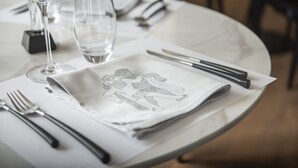 Une table dressée avec une serviette pliée ornée d’une illustration romantique, un verre à vin et des couverts.