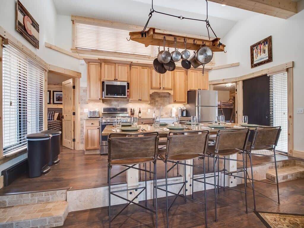 Une cuisine spacieuse avec des meubles de rangement en bois, un îlot central doté de tabourets et un porte-ustensiles suspendu.