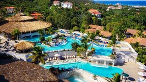 A resort with multiple swimming pools, palm trees, and a thatched-roof structure. - You Will Forever Be My Always (Puerto Plata)