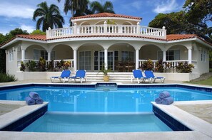 A pool with blue tiles, white columns, and blue lounge chairs.