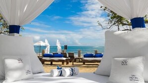 A beachside lounge with white canopies, blue cushions, and a view of the ocean. - Happy As A Clam (Puerto Plata)